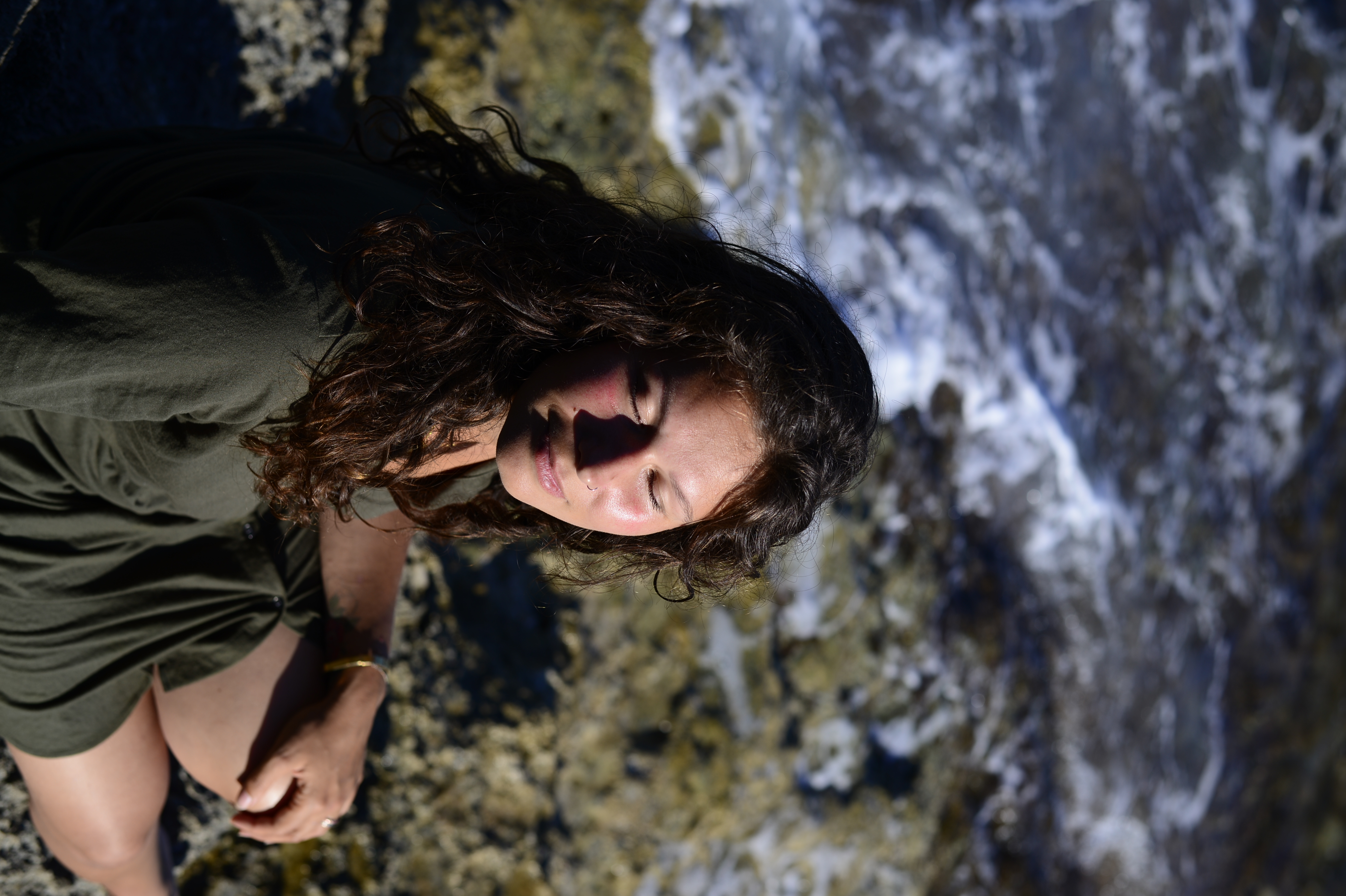 Nikita sitting on the Salento rocks, eyes closed, sun on her face, the sea behind her
