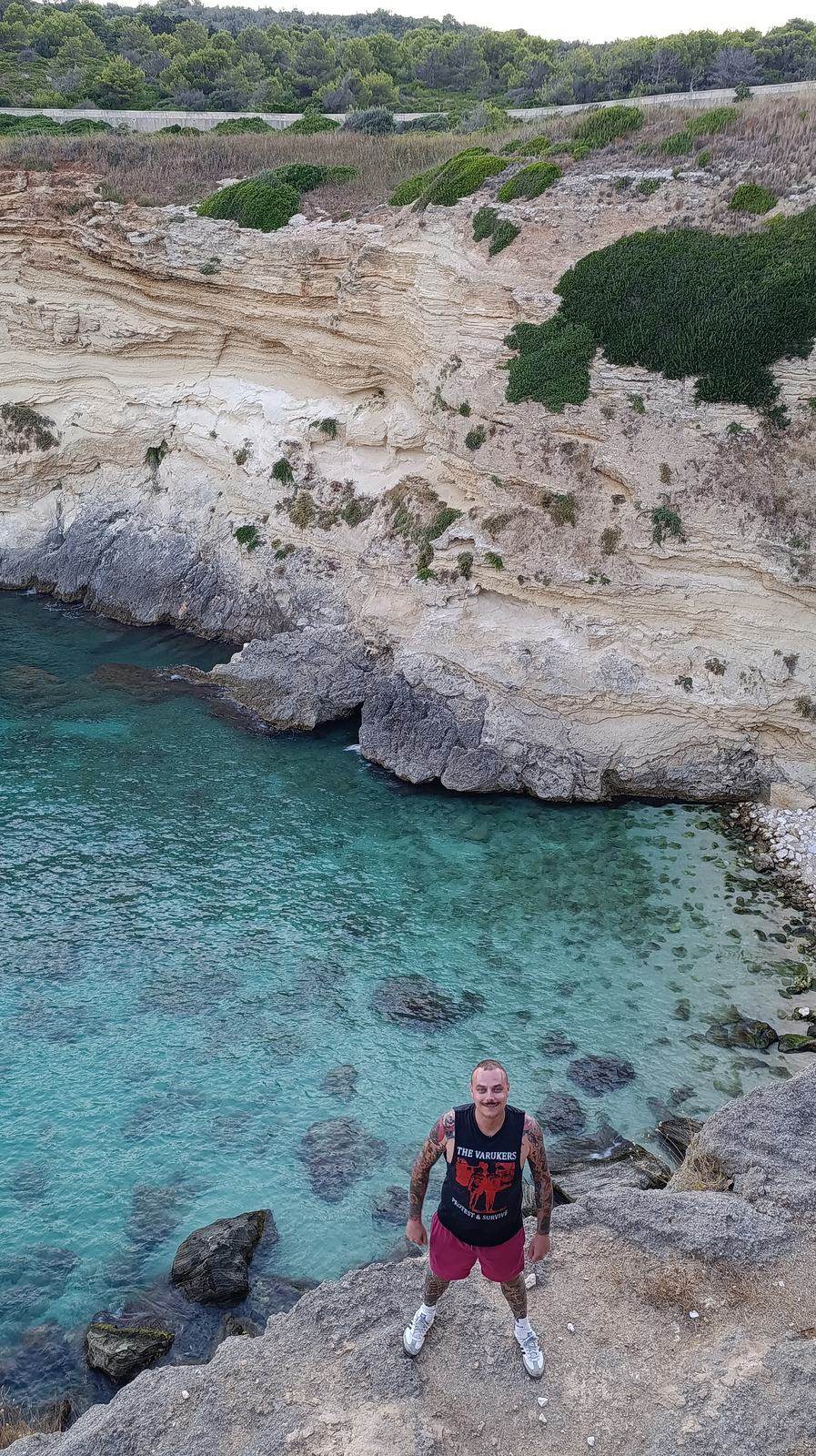 Moritz standing on the white cliffs above turquoise water along the Salento coast