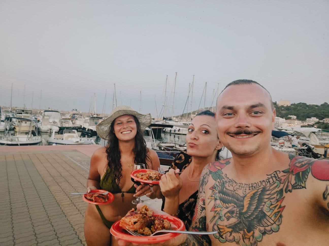 Nikita, Valentina and Moritz smiling together at the marina, eating fresh fish after a day on the boat