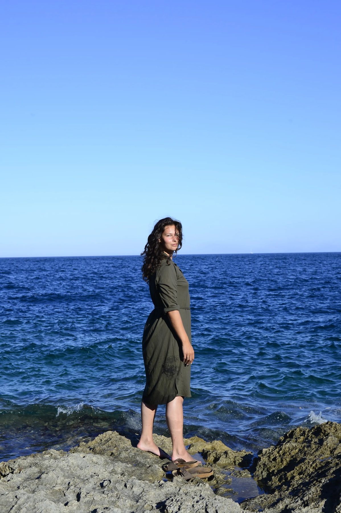 Nikita in green dress standing on Salento rocks, the Adriatic behind her