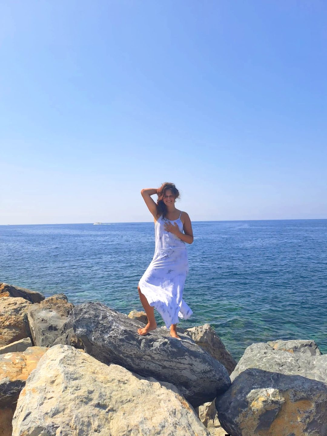 Nikita in white dress on rocks by the sea in Liguria, the land of her mother