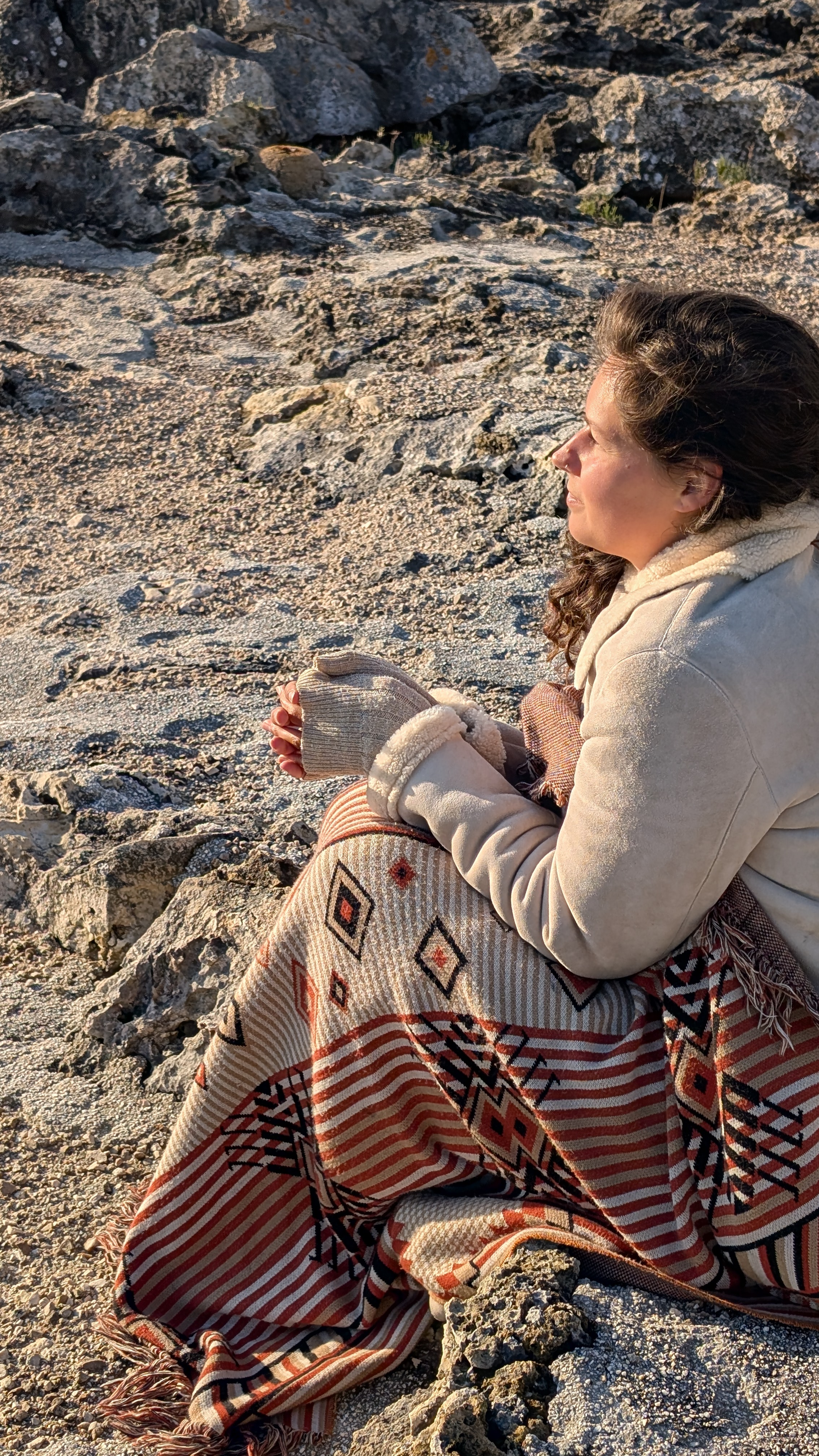 Nikita wrapped in blanket on Salento rocks at sunrise holding a warm cup