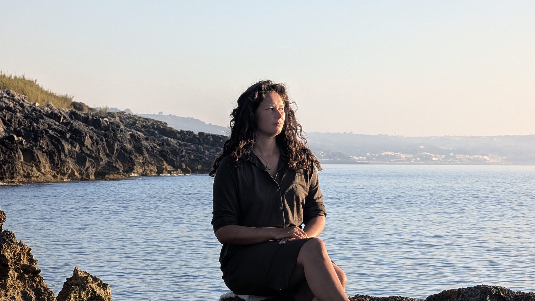 Nikita sitting on rocks by the sea in Salento at sunrise, looking out to the horizon