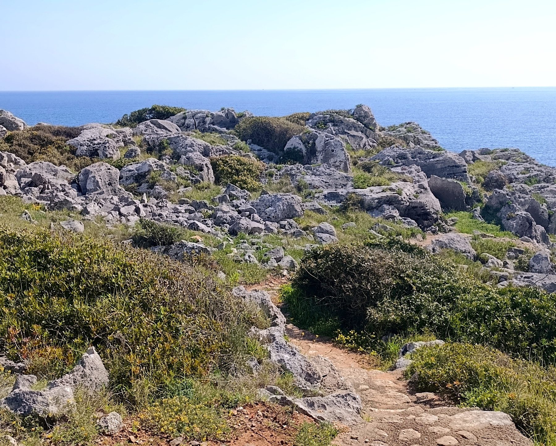 Stone path through Salento scrubland leading toward the sea and horizon