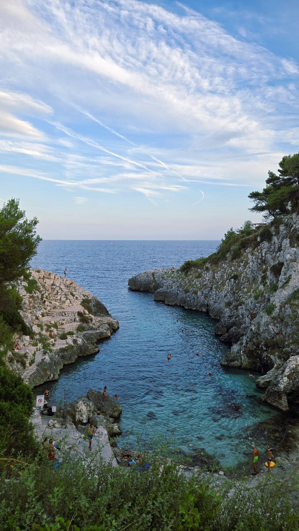 Una stretta insenatura sulla costa salentina con scalini scavati nella roccia e persone che nuotano