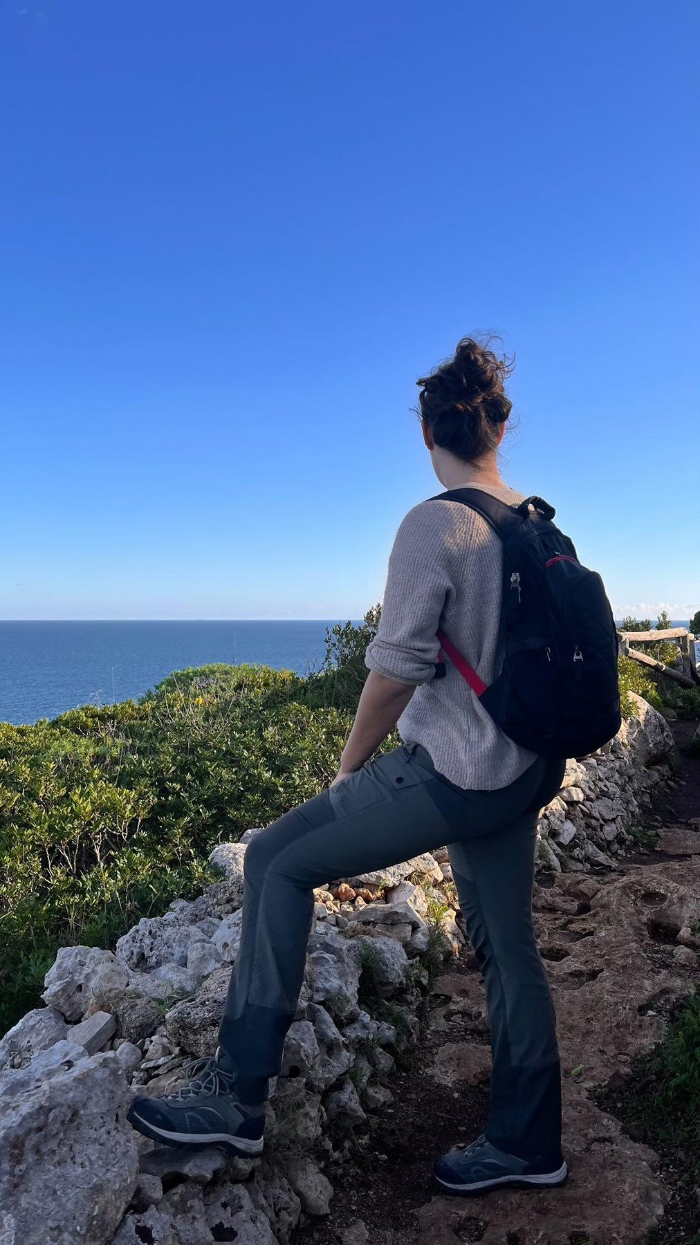 Nikita on the cliff path above the sea in winter, wearing a sweater, Salento