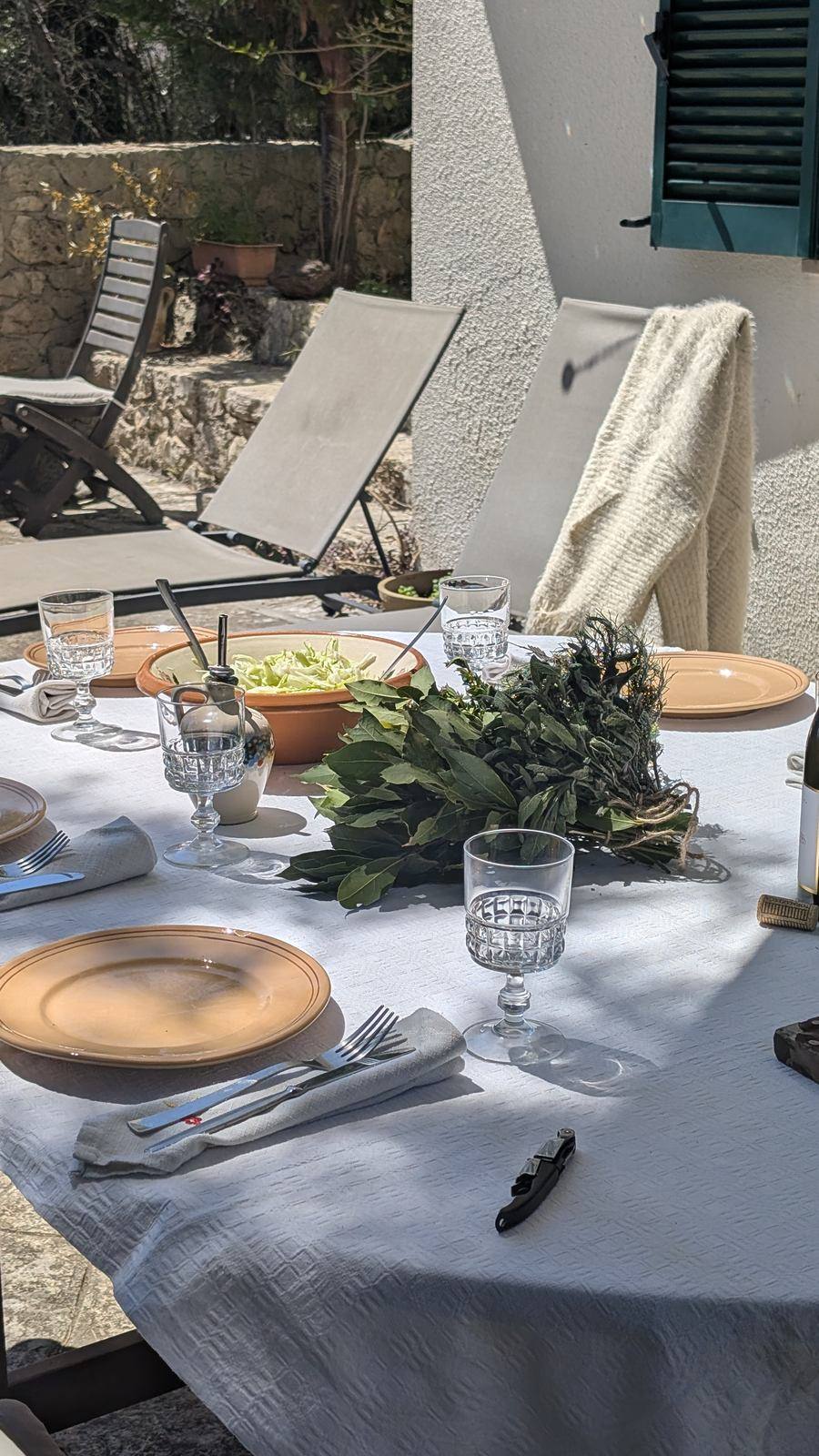 Tavola apparecchiata sul terrazzo, con erbe fresche al centro
