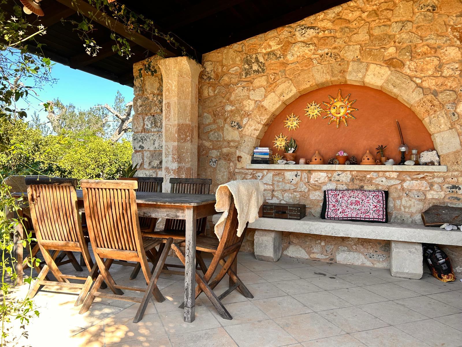 The covered terrace at Il Sentiero with a wooden table, a stone bench and ceramic suns in an arched niche
