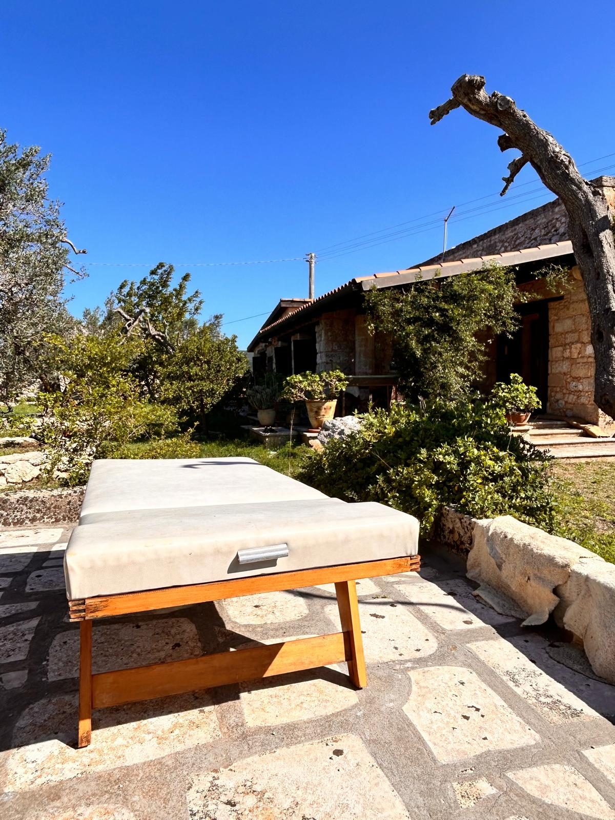 A wooden treatment table on the stone terrace in the garden at Il Sentiero, with olive trees and the house behind
