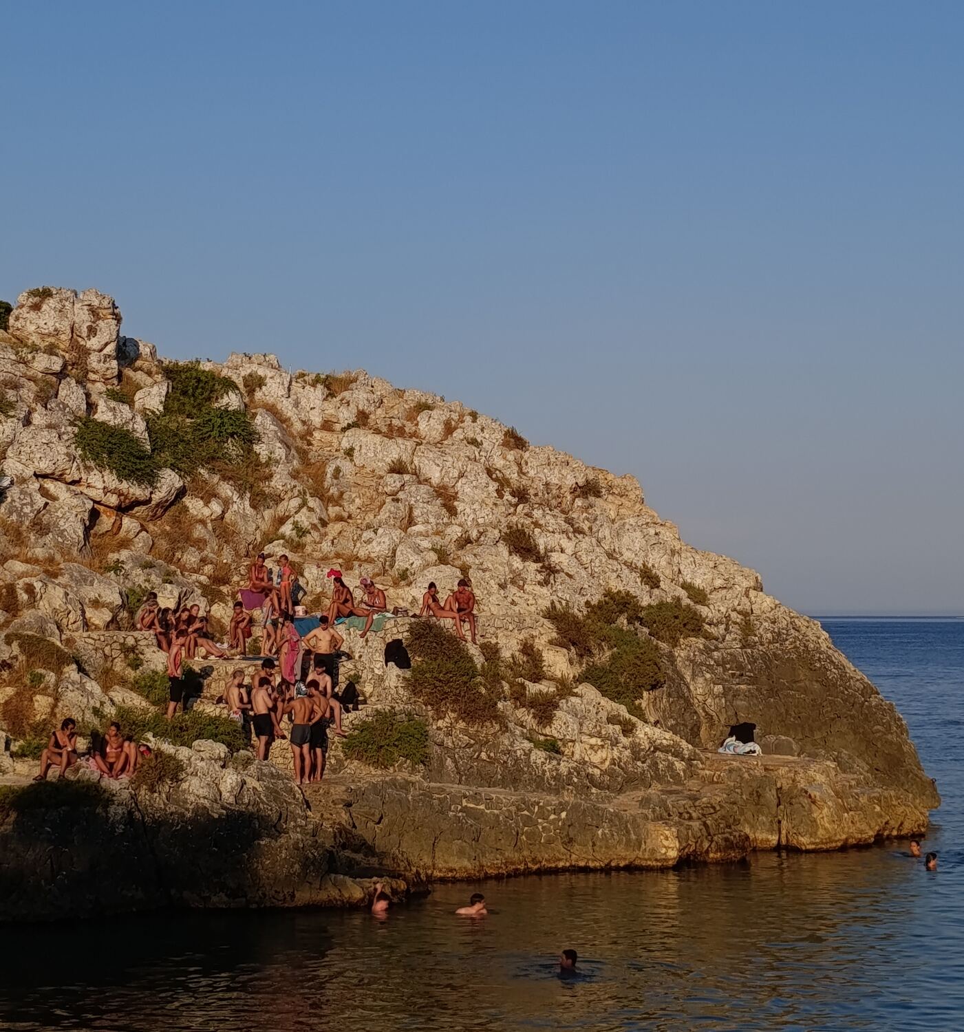 Locals swimming and sunbathing on the rocks at golden hour, Salento